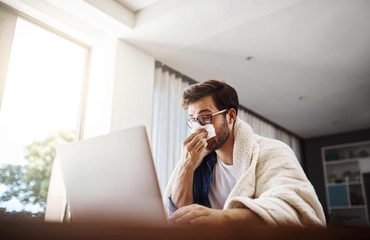 Shot of a sickly young businessman blowing his nose with a tissue while working from home