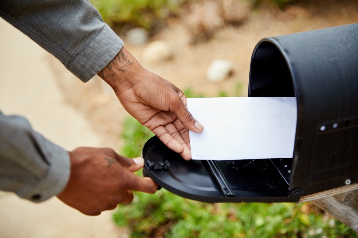 man standing outside of his house and removing an envelope from his mailbox