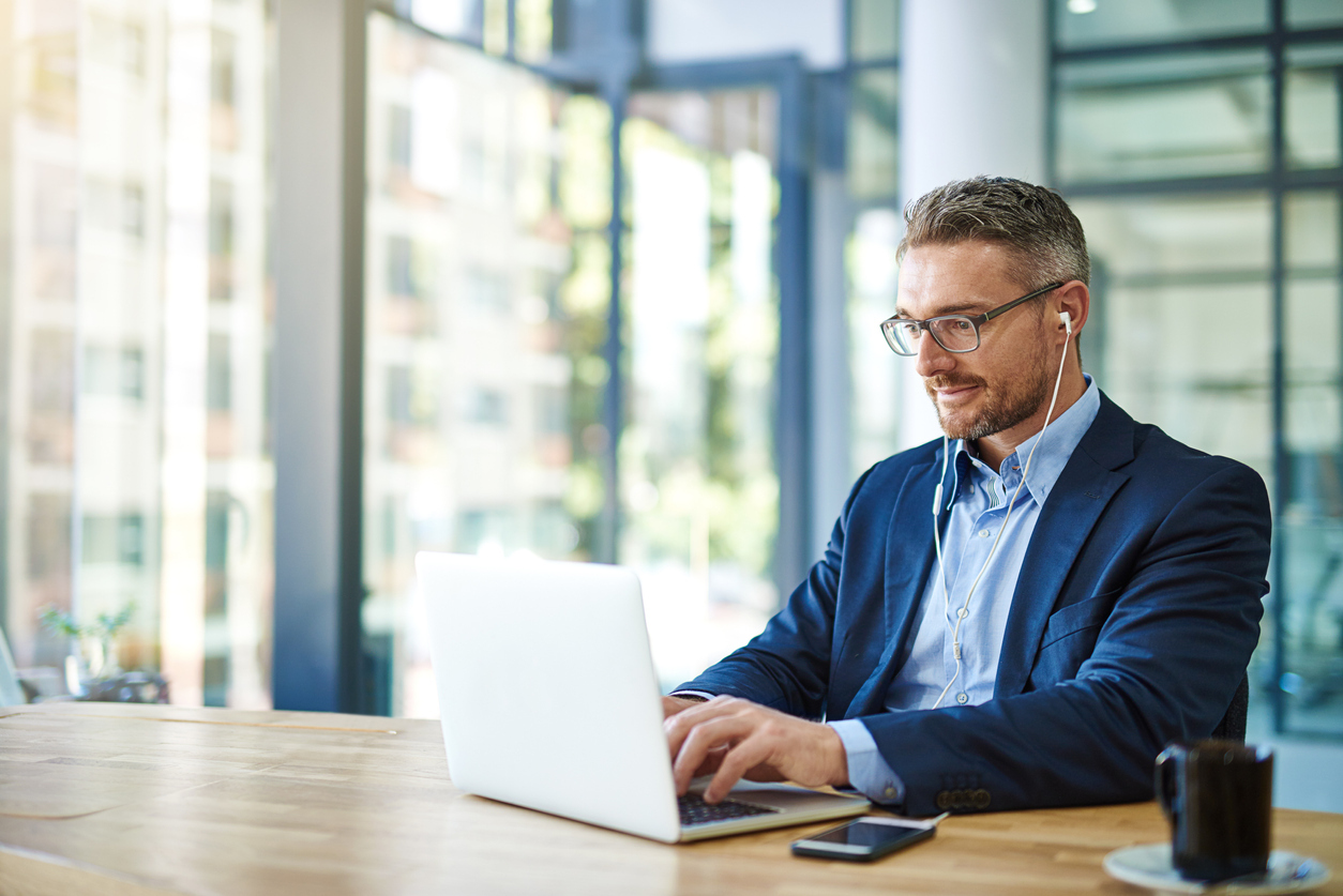 Shot of a mature businessman wearing earphones while using his laptop at work