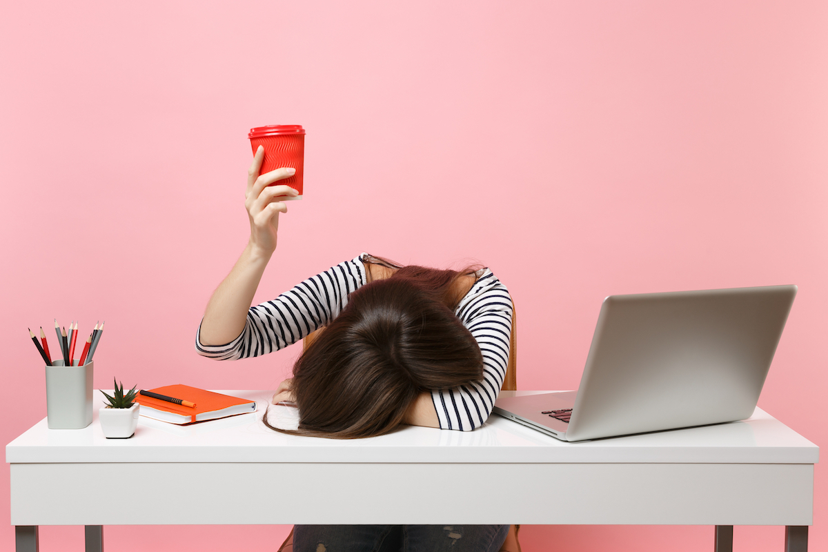 Tired woman with head on desk holding coffee