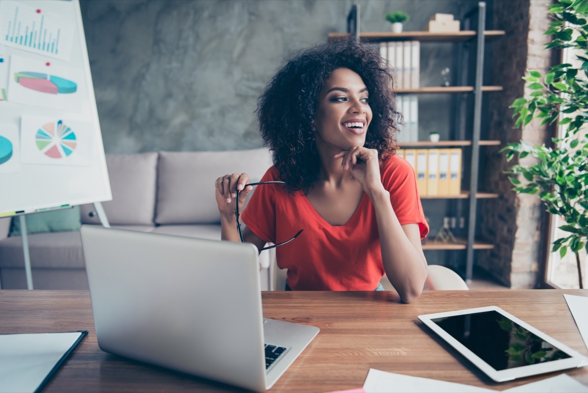 young black woman looking out window while working on laptop