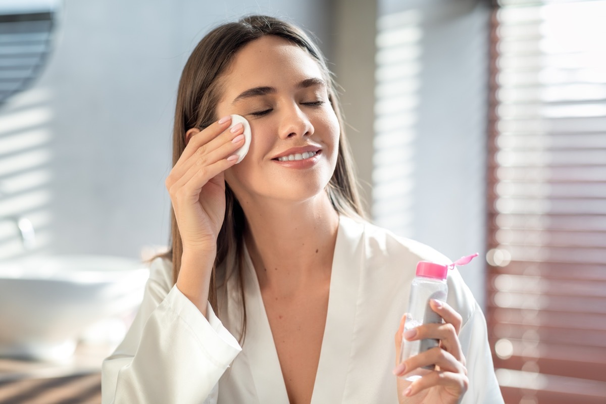 Smiling woman uses micellar water on her face