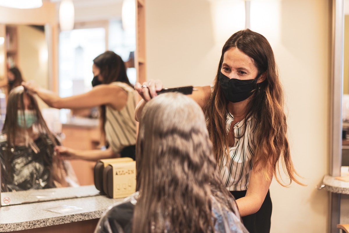 happy smiling woman hairdresser coiffeur cutting womans long hairs during first weeks of reopening in times of covid-19 crisis