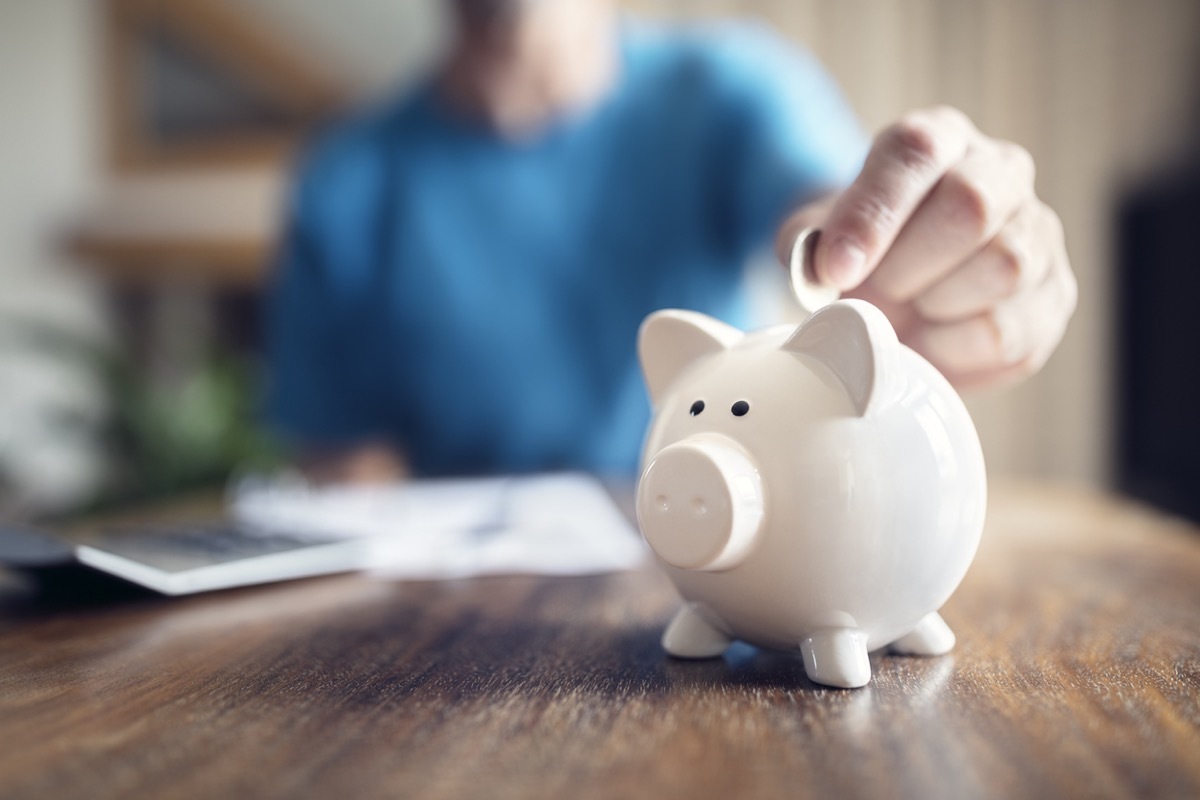 Close up of a person putting a coin into a white piggy bank