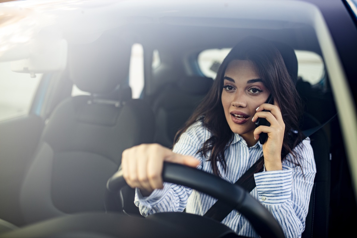 Woman In Car Talking On Mobile Phone Whilst Driving. Attractive woman uses smart phone while driving.