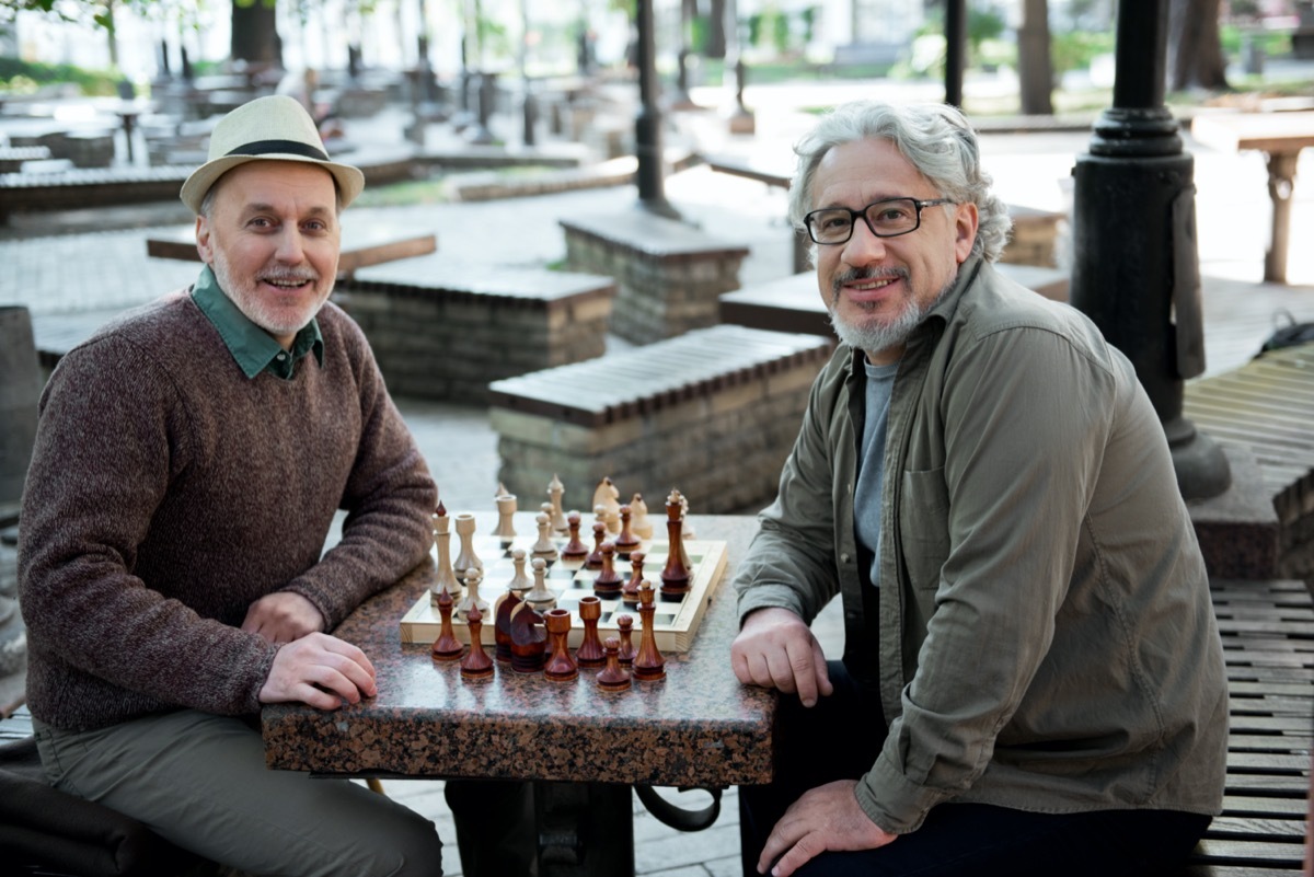 Glad mature pensioners relaxing near chessboard in park