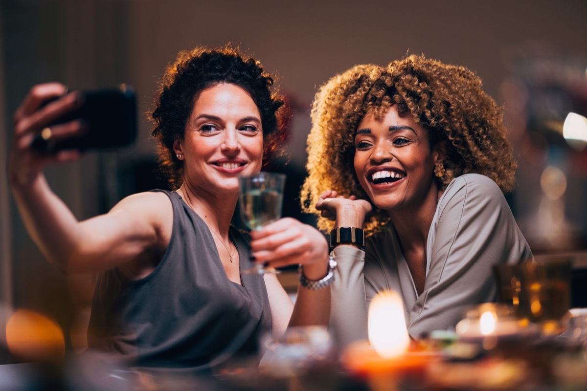 Cheerful smiling woman taking photography on a mobile phone with her friend during a dinner party.