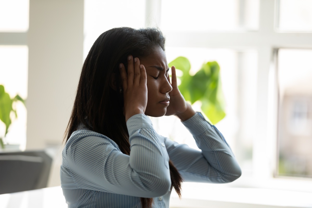 Young woman holding her head as though she has a headache while in the office