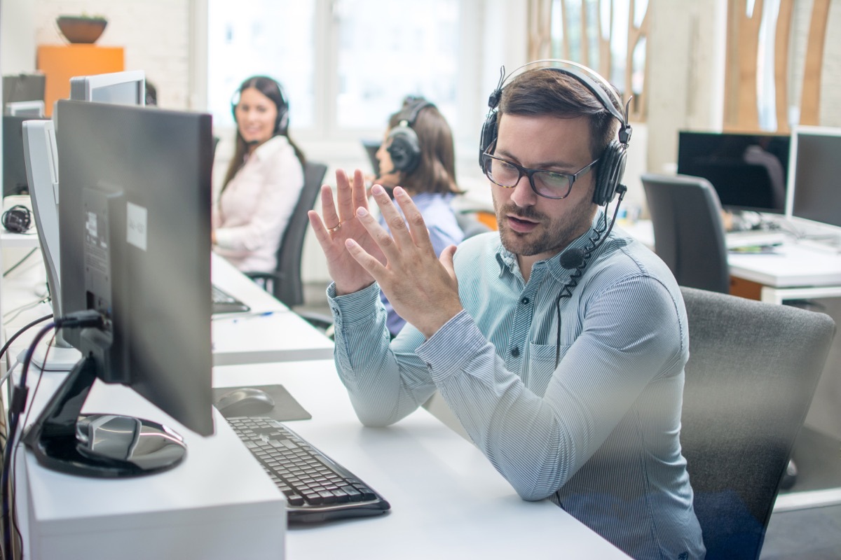 Male technical support agent trying to explain something to a client while using hands-free headset at call center.