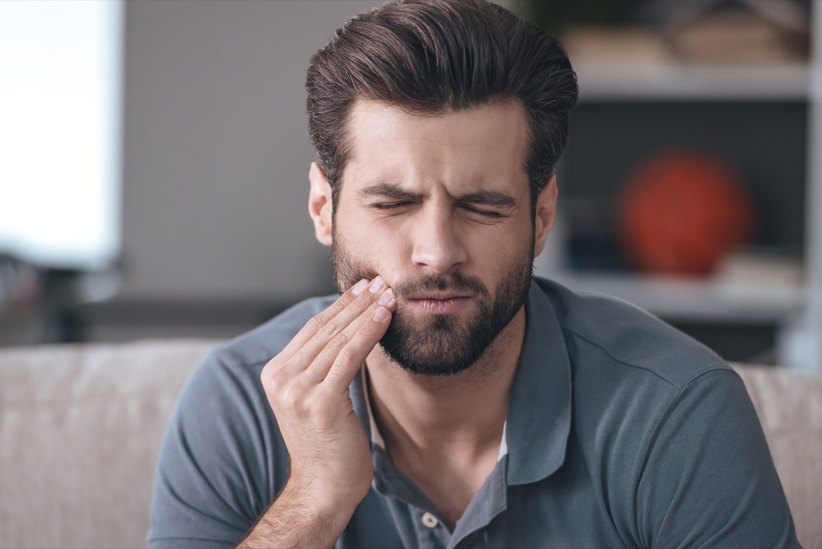 Toothache. Frustrated young man touching his cheek