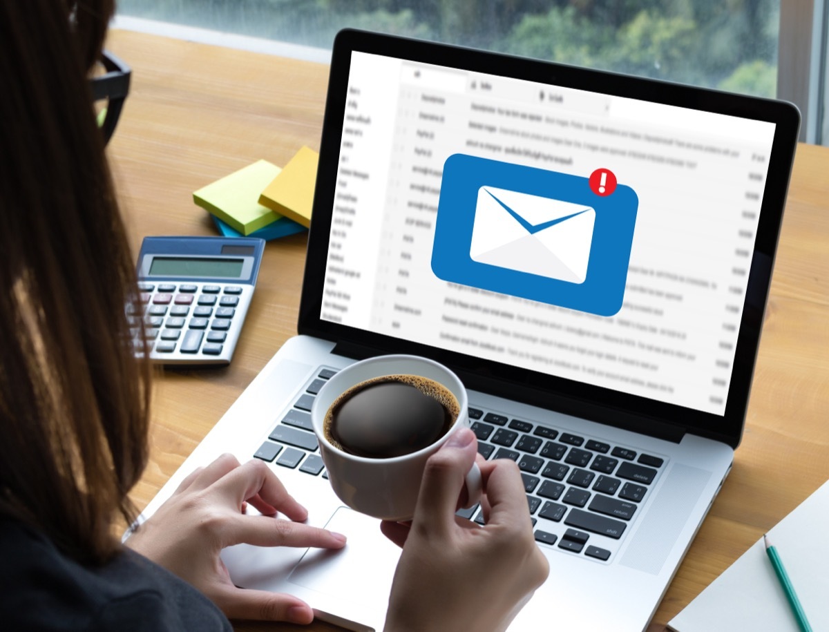 top view of a woman holding a cup of coffee while using her laptop with an email notification on it