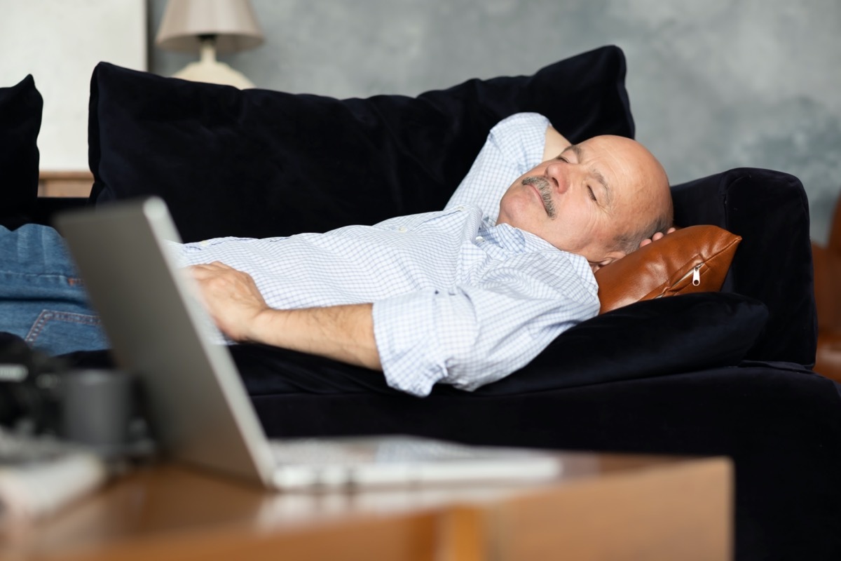 Tired senior hispanic man sleeping on dark blue couch, taking afternoon nap at the living room