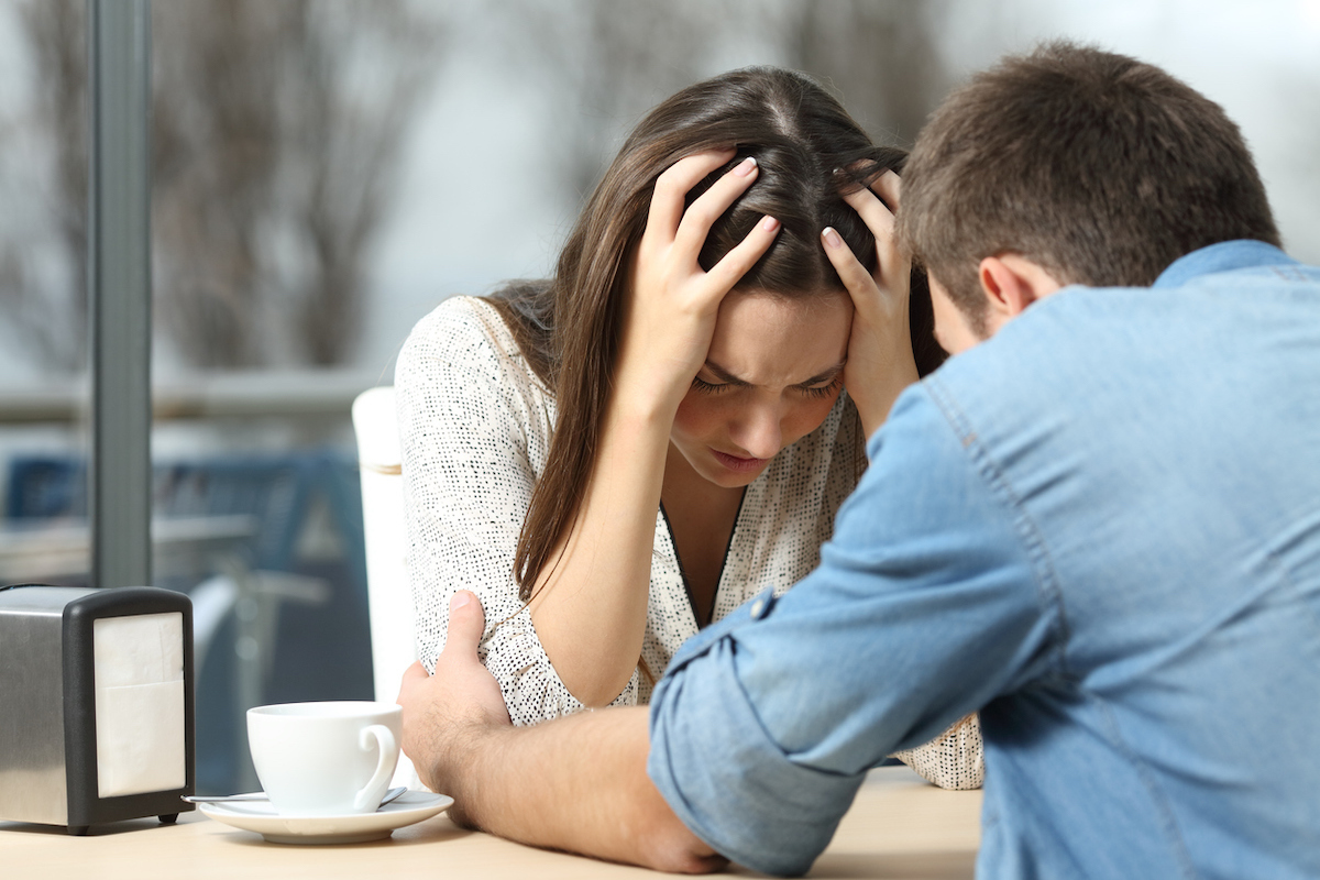 A man comforting his needy, sad female partner at a restaurant table.