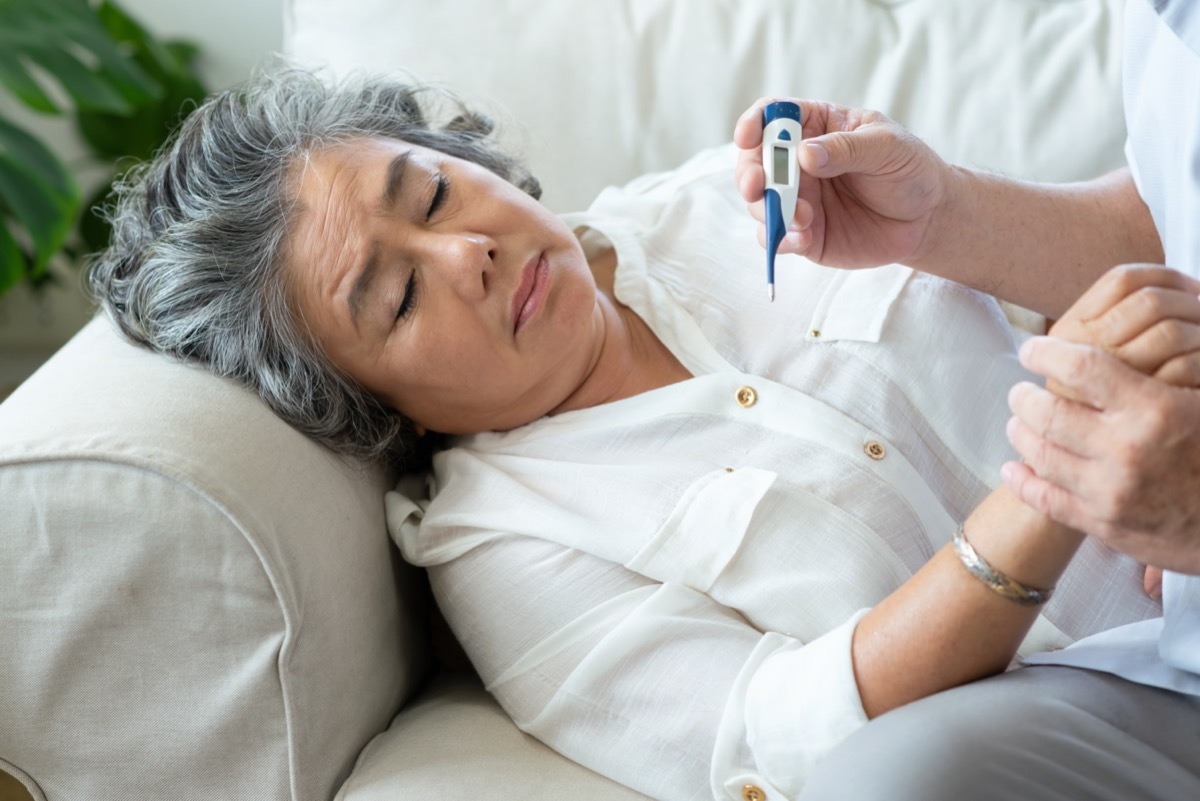 Elderly woman having cold during lie down on couch while Senior man checking temperature of his wife with digital thermometer in house