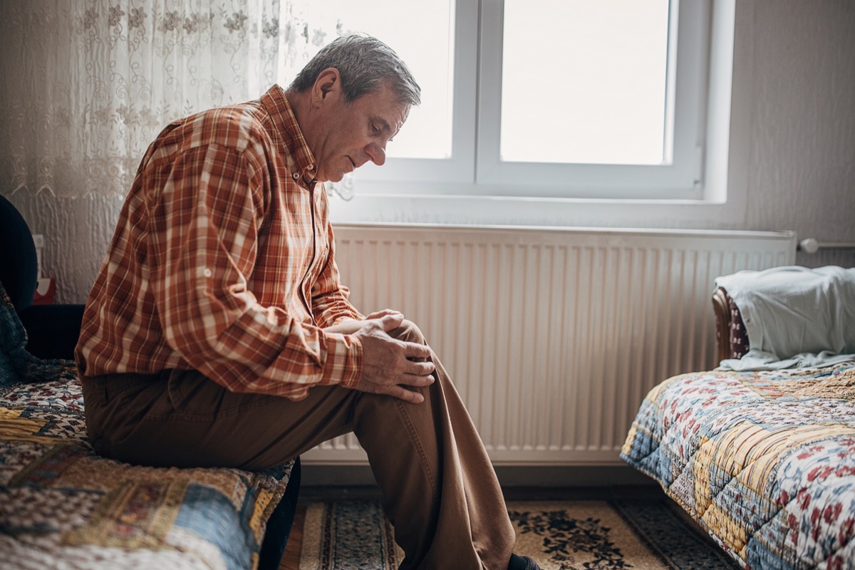 One man, worried senior man, sitting alone at his home. He has a pain in his knee.