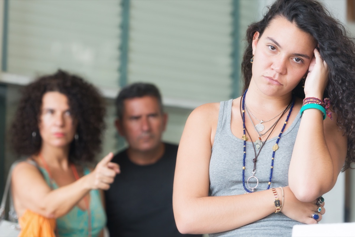 annoyed teenage daughter standing there while her parents yell at her