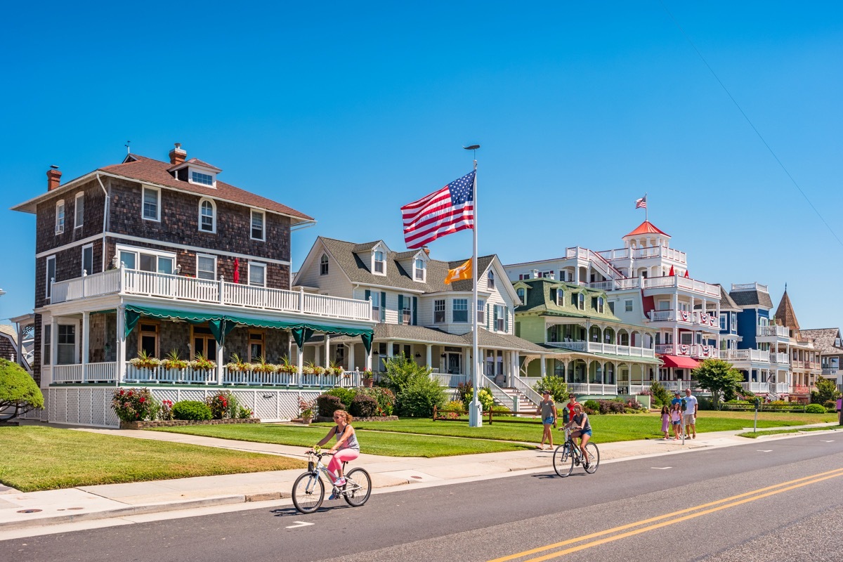 People bike and walk in front of traditional villas in Cape May, New Jersey, USA, on a sunny summer day.