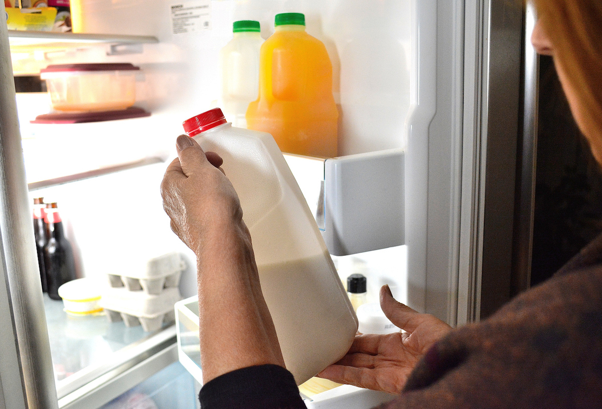 closeup of person looking at bottle of milk with open fridge door