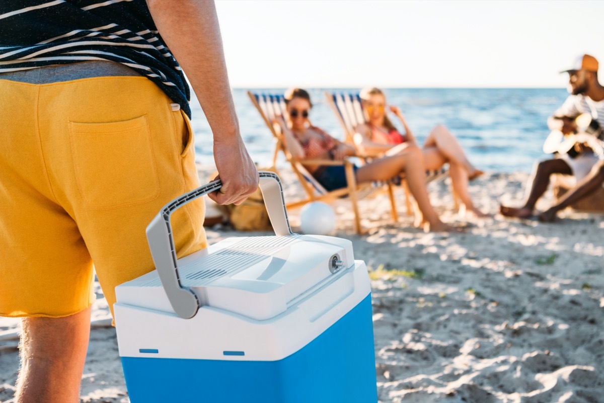 man in yellow trunks holding cooler on the beach