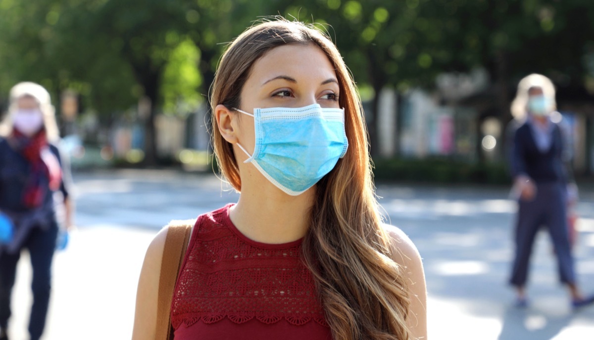 Social Distancing Woman in city street wearing surgical mask against disease virus SARS-CoV-2.