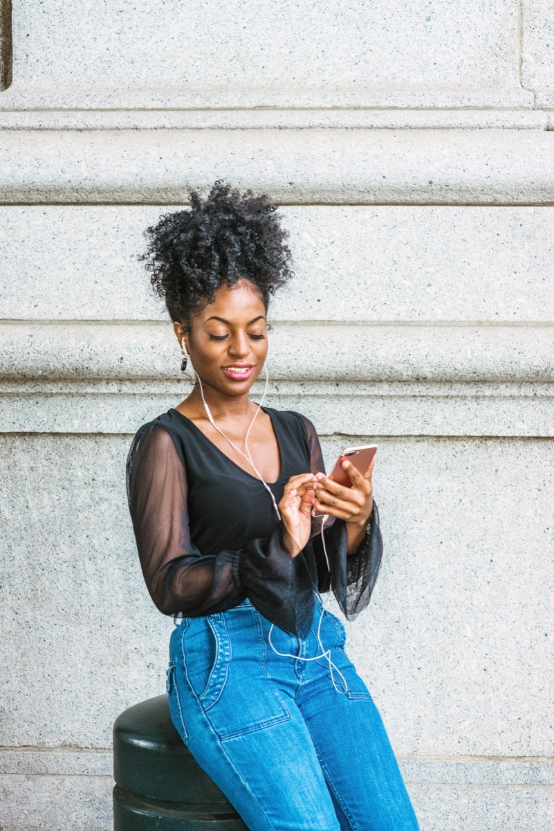 Woman texting and listening to music wearing a black shirt with sheer sleeves