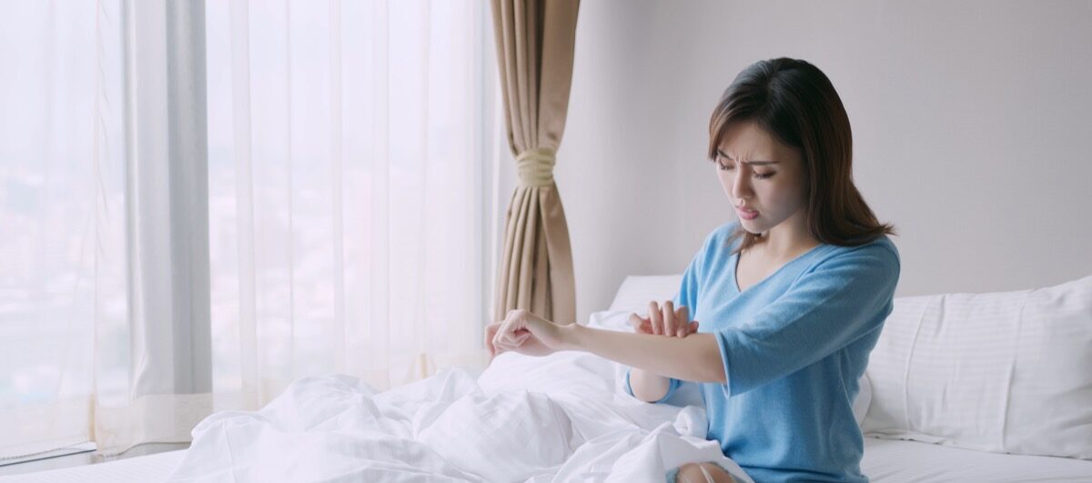 Woman scratching arm in bed from bug bite