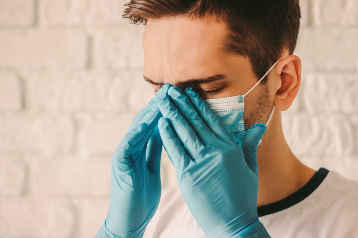 Frustrated tired man in protective gloves on hands and medical face mask feeling headache.