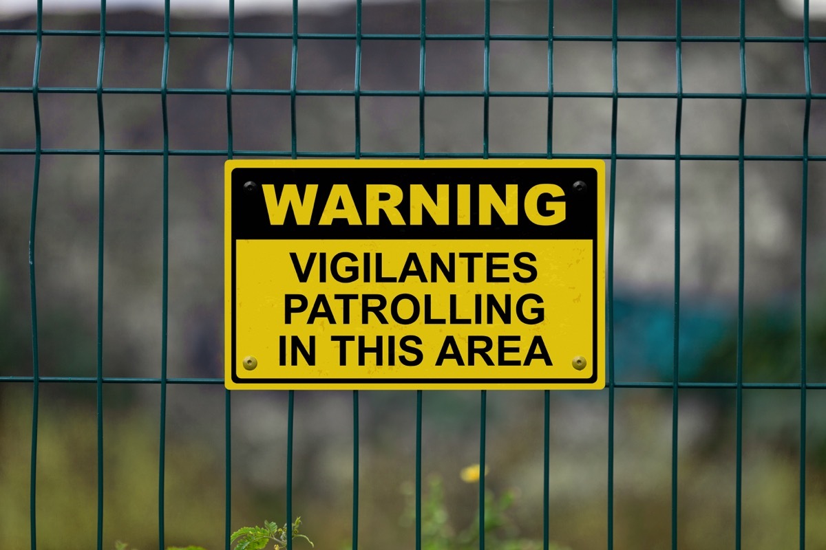 Red an white warning sign on a fence stating in 