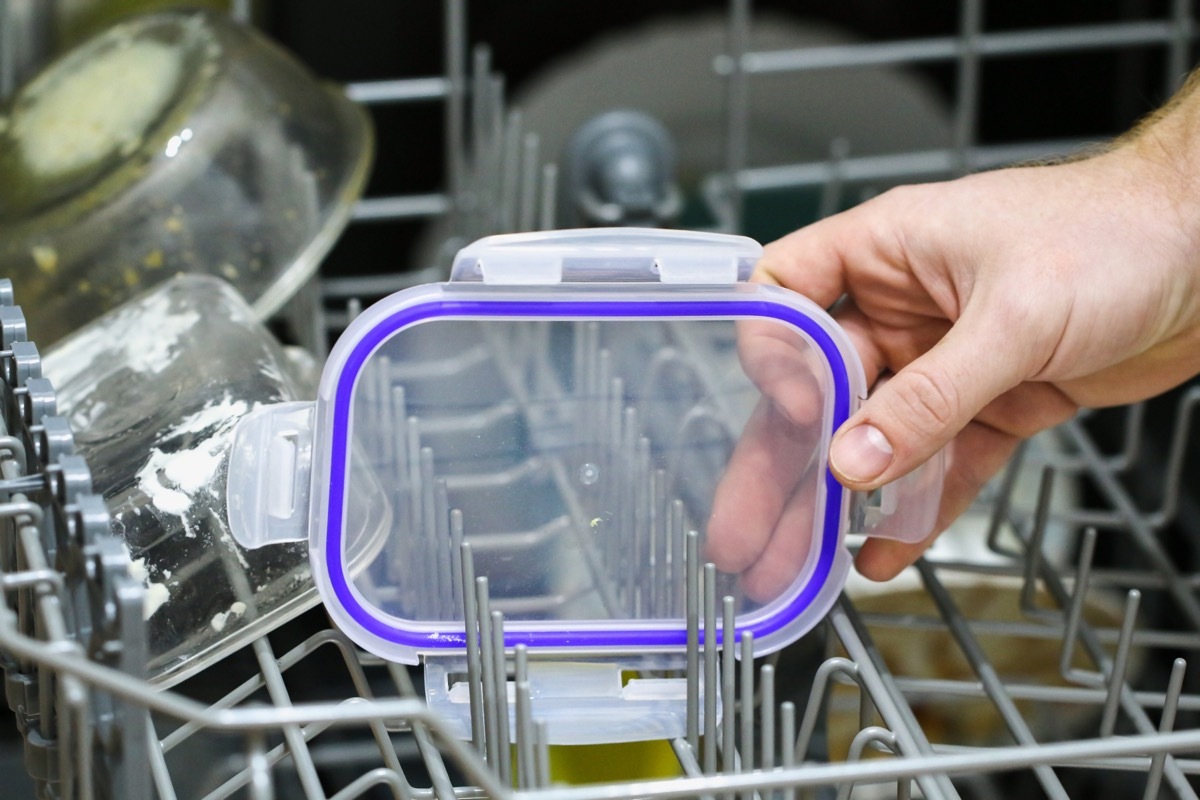 A man loads dirty dishes, plates, spoons, forks, cutlery into the dishwasher tray.