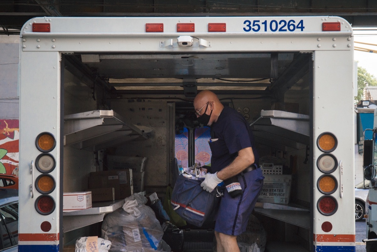 A mail man waring a face mask inside a truck getting ready to deliver.