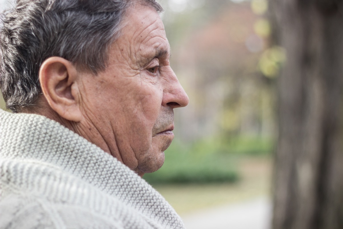 Portrait of a pensive senior man sitting on the bench, in the public park, outdoors. Old man relaxing outdoors and looking away. Portrait of senior man looking thoughtful