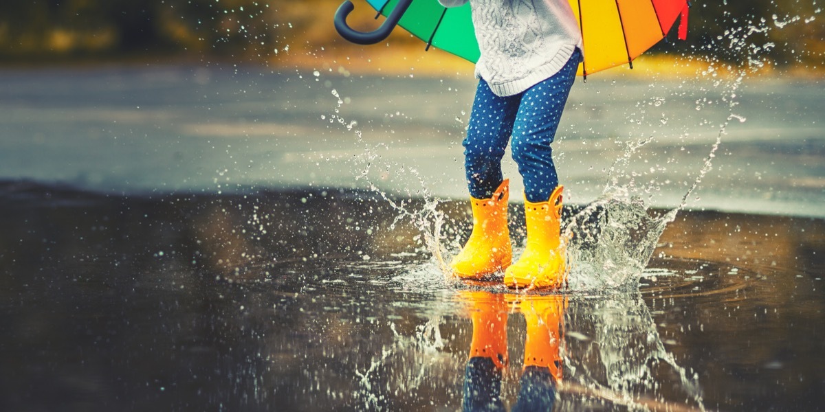 Feet of child in yellow rubber boots jumping over a puddle in the rain - Image