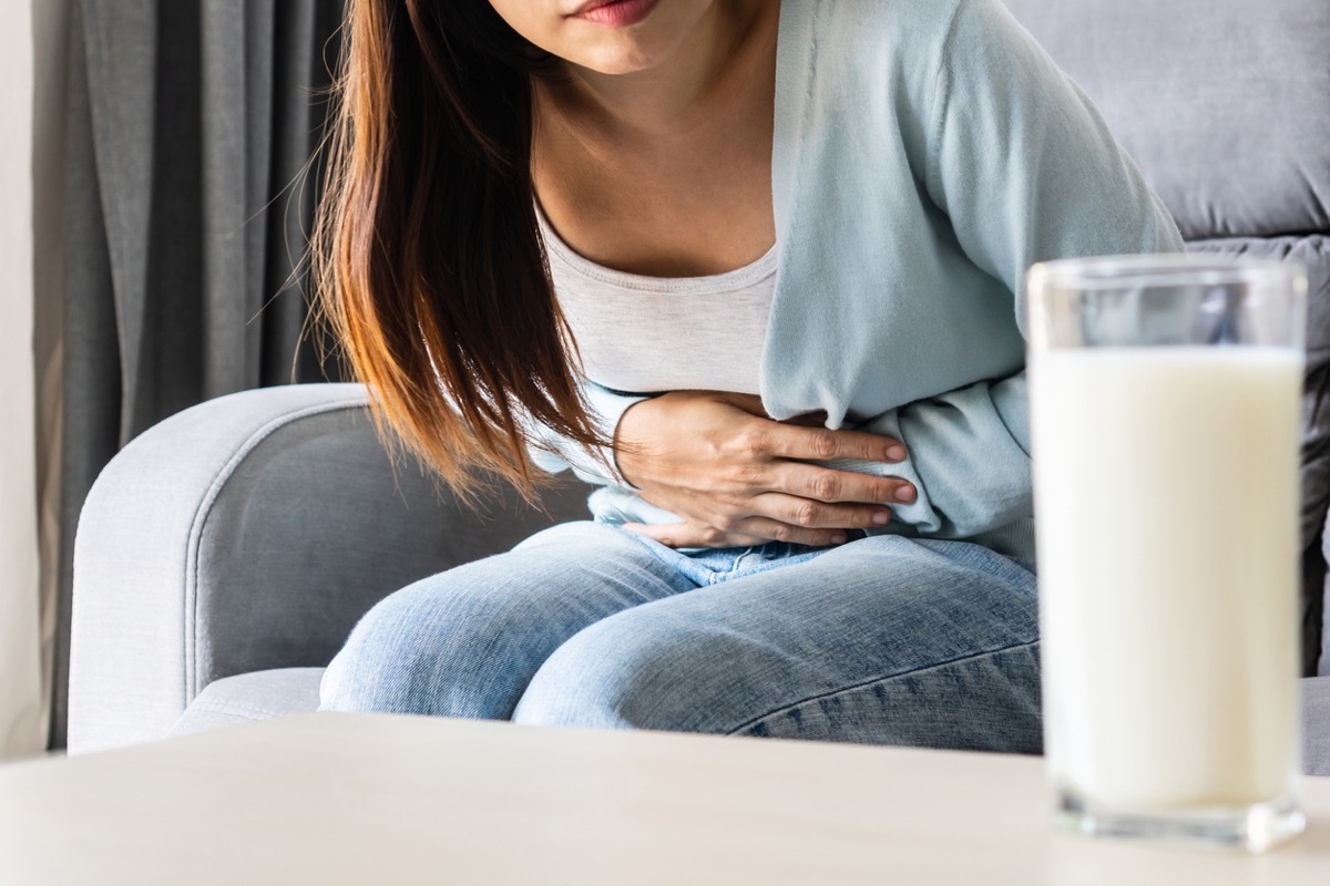 Unhappy young woman having bad stomach ache with glass of milk on table. Lactose intolerance, food allergy concept. Close up, copy space