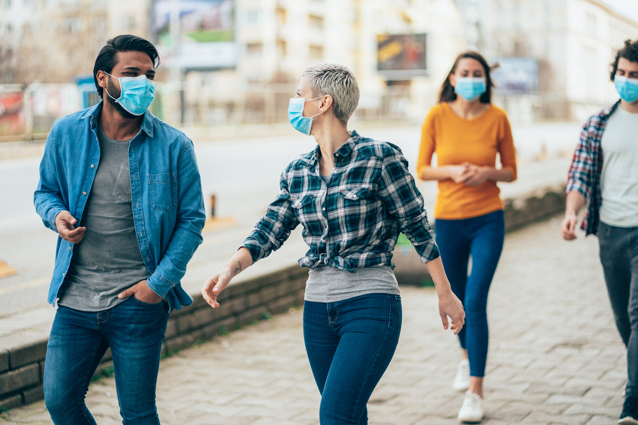 A group of young people walking down the street while wearing face masks.