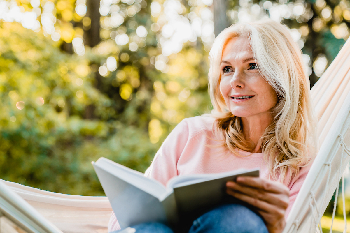 Beautiful,Senior,Blonde,Woman,Reading,Book,And,Sitting,In,Hammock