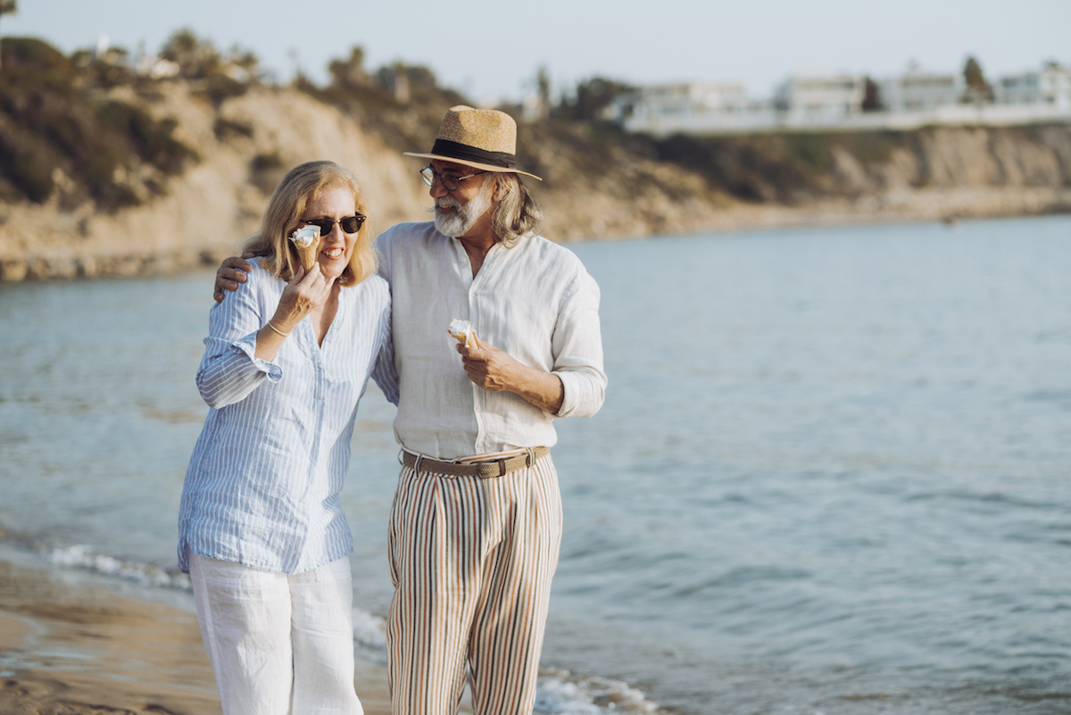 Happy mature couple walking by the sea, eating ice cream