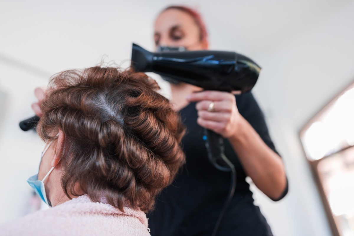 Hair dresser and old woman at hair parlor during hair stylizing