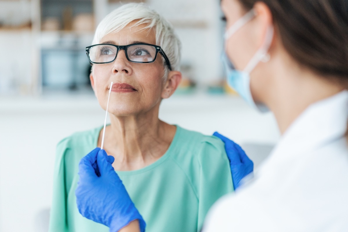 Doctor with protection gloves doing Coronavirus nasal swab test on senior female patient