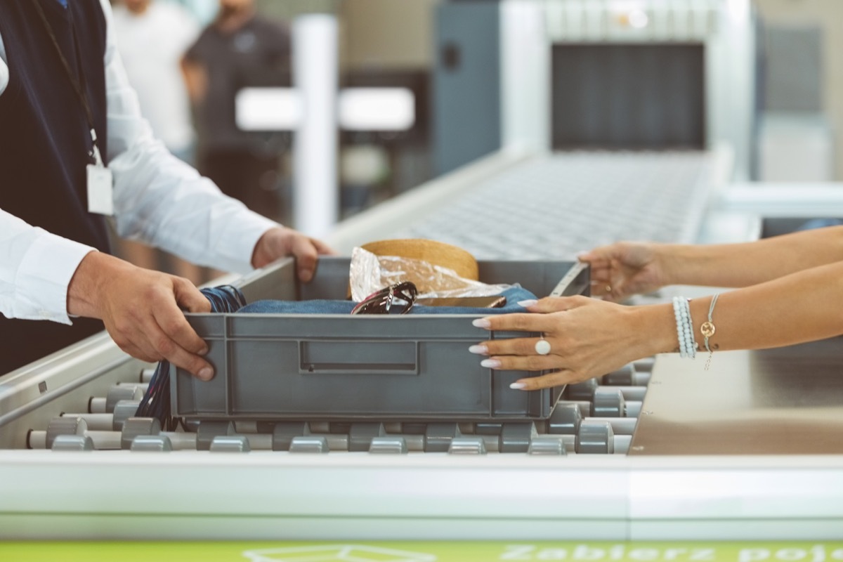 Woman giving container of personal accessories to security guard at airport