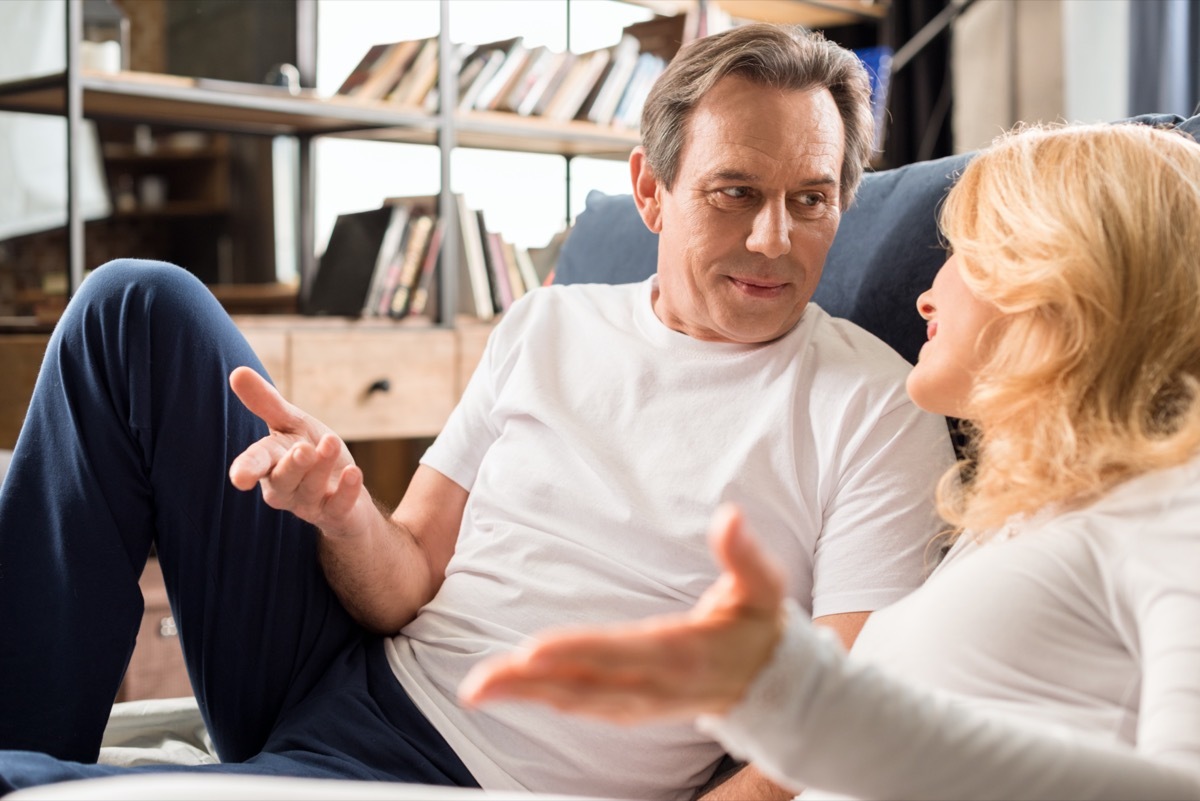 Happy middle aged couple talking and lying on bed at home