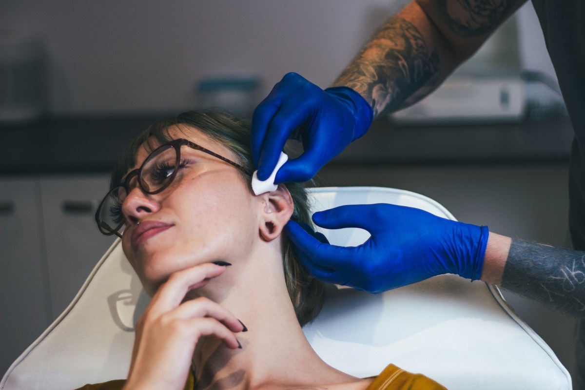 Young Woman getting her ear pierced. Man showing a process of piercing with steril medical equipment and latex gloves. Body Piercing Procedure (Young Woman getting her ear pierced. Man showing a process of piercing with steril medical equipment and la