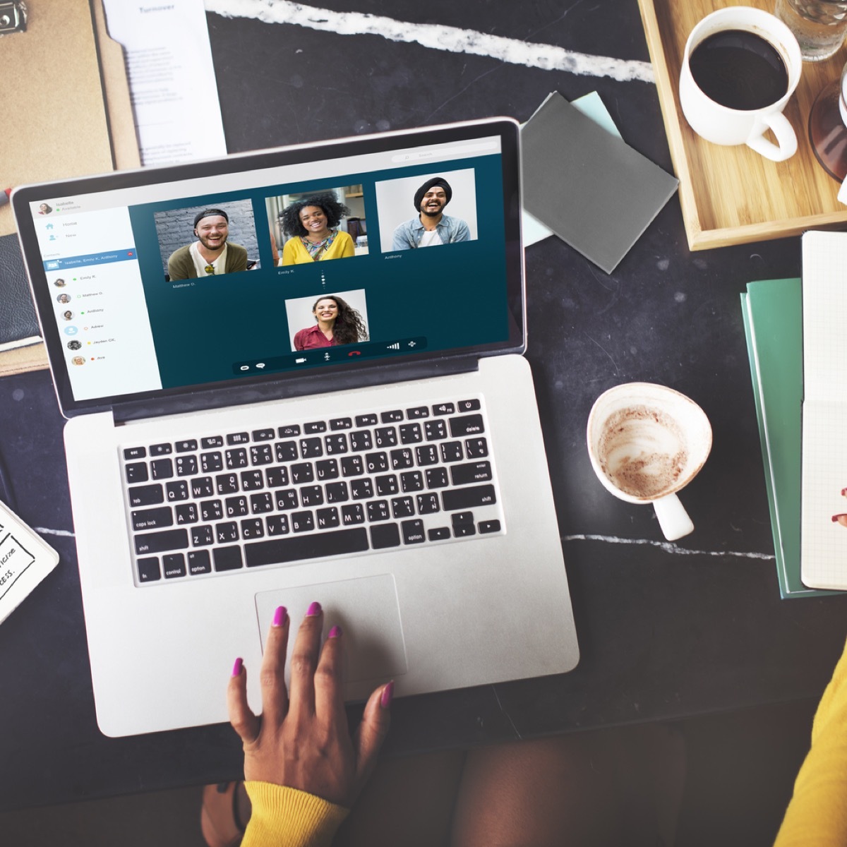 close up of woman's hand on computer while video chatting with four other people