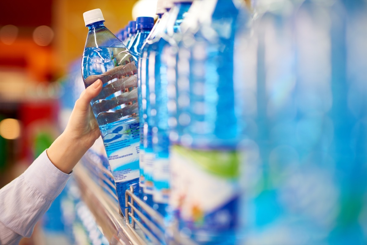 Female hand taking bottle of mineral water from supermarket shelf