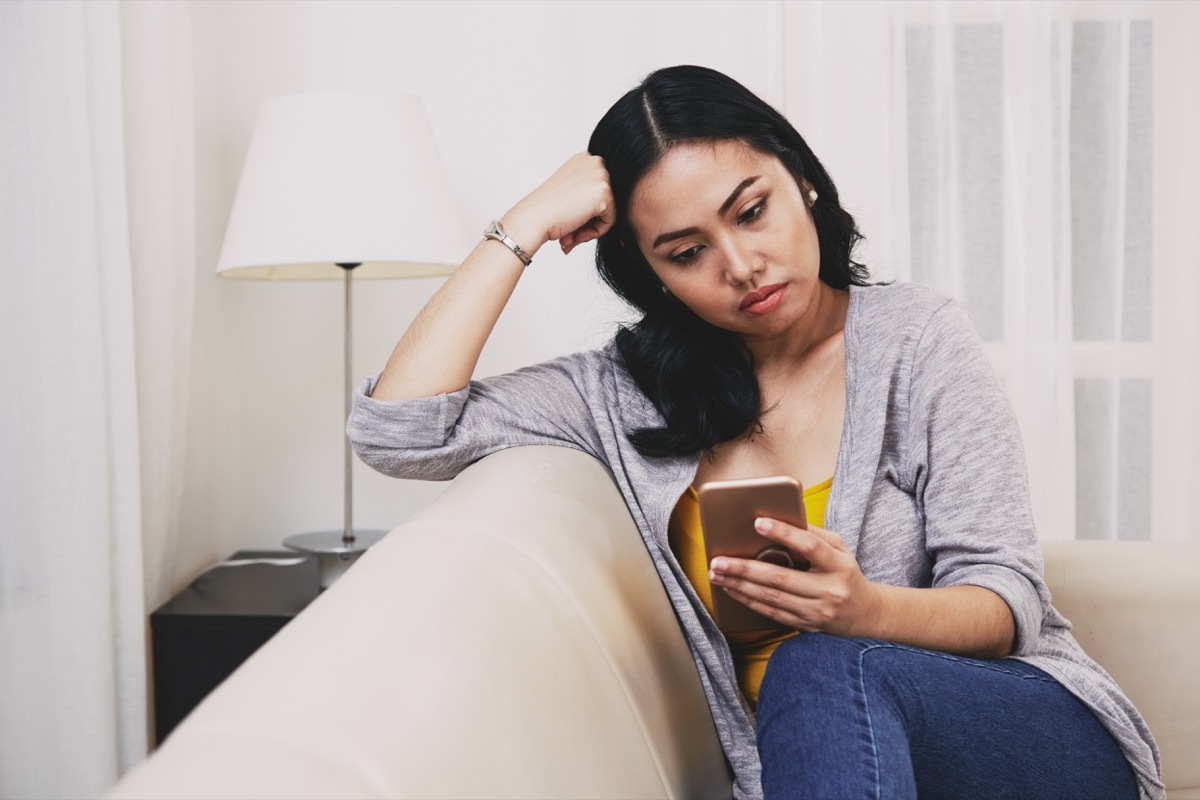 sad pensive young Filipino woman reading text messages or news on smartphone