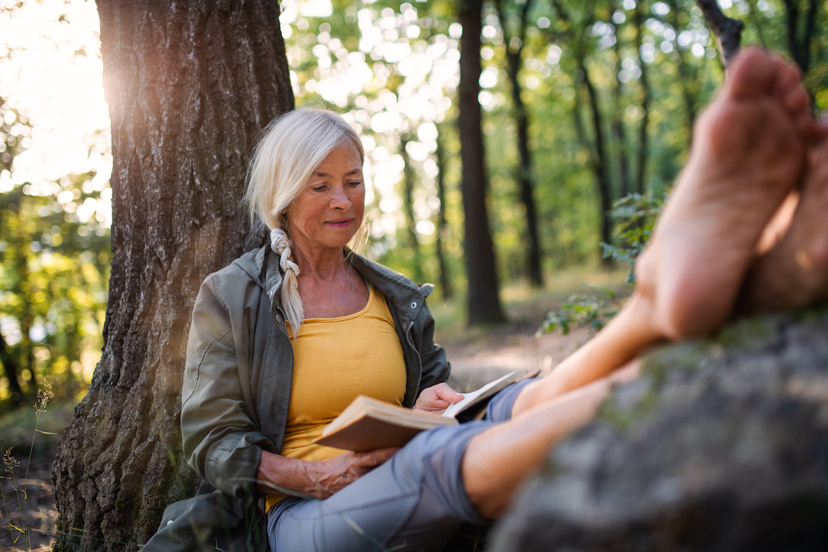 older asian woman reading by tree