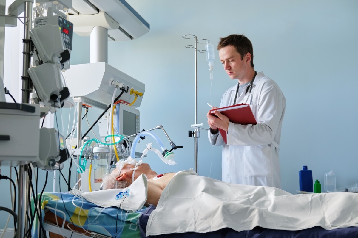 Intensive care caucasian doctor examines intubated critical stance patient writing notes to case report in intensive care department