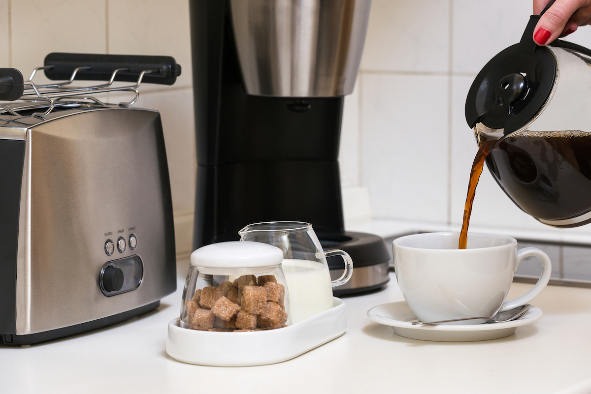 A hand pouring coffee in a cup with a tray of milk and sugar on the counter