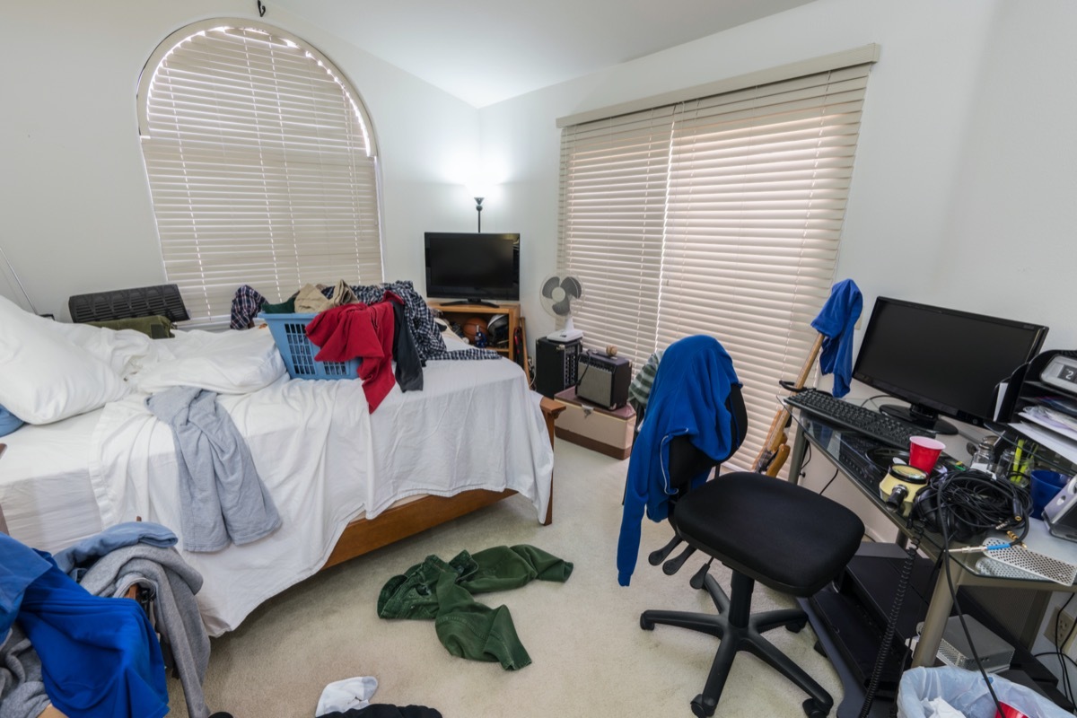 Cluttered, messy teenage boys bedroom with piles of clothes, music and sports equipment.