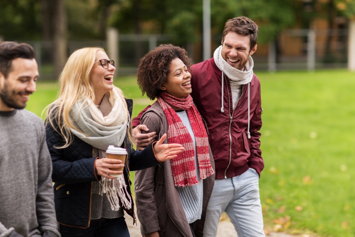 group of happy friends with coffee walking along autumn park and laughing