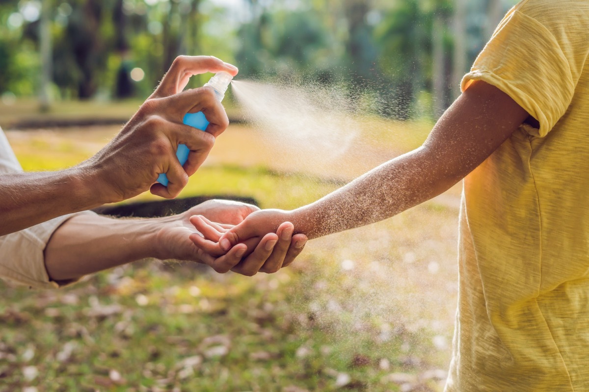 person spraying child's arm with aerosol sunscreen